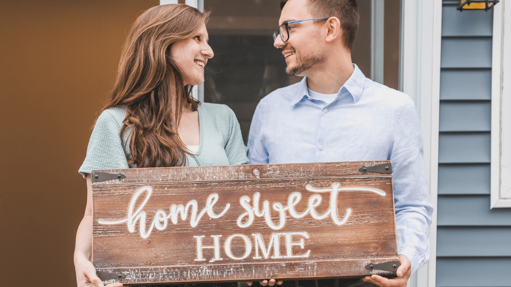 New homeowners holding a sign that says "Home Sweet Home"